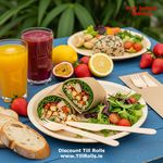 Compostable 3 in 1 wooden cutlery set with fork, knife, and napkin beside plates of food and glasses of cola on an outdoor picnic table.
