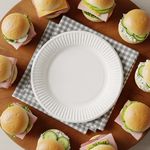 A  compostable 9-inch white paper plates resting on a background of green leaves, representing a sustainable choice for eco-conscious businesses