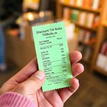 Image of a customer holding a green credit card receipt supplied by Discount Till Rolls in a book store  settiing